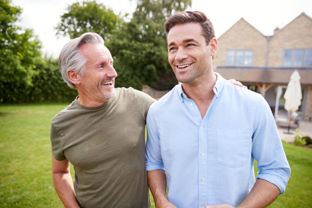 Senior Father And Adult Son Walking And Talking In Garden Together